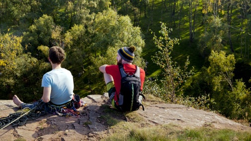 Two climbers sitting on top of cliff overlooking trees